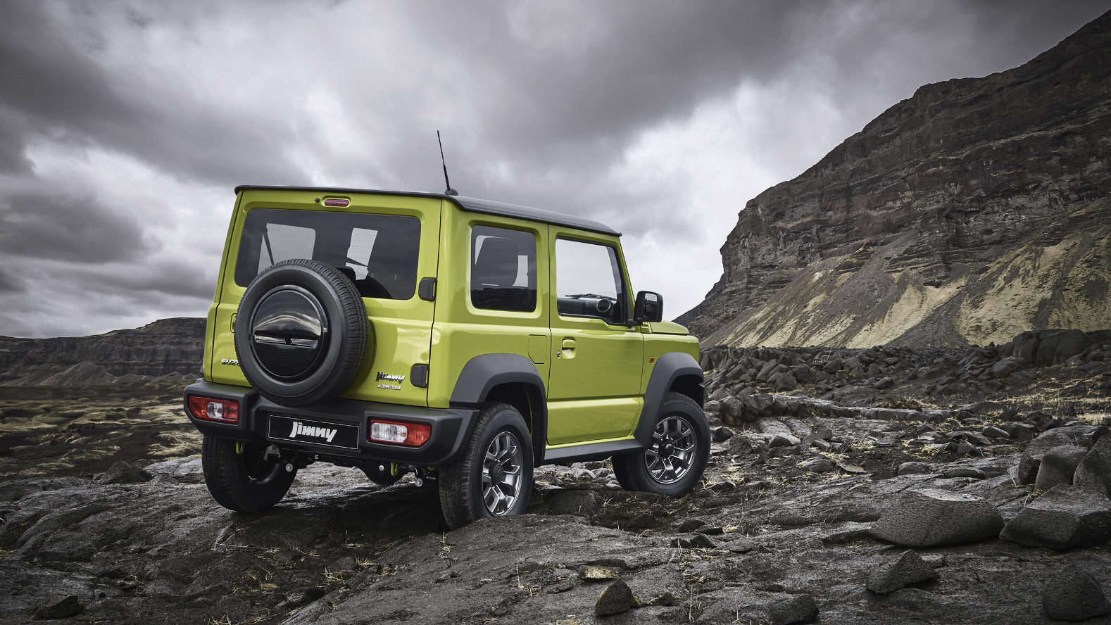 A yellow-green Suzuki Jimny from behind driving on a rocky outcrop.